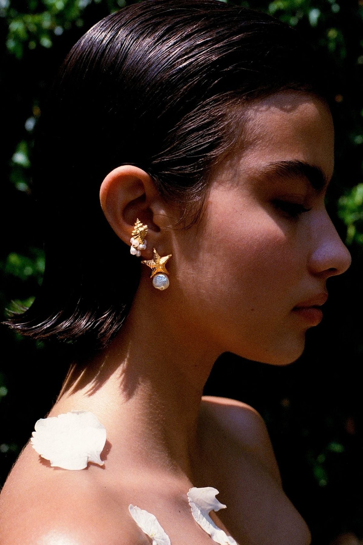 Woman wearing gold earrings with a blurred green background