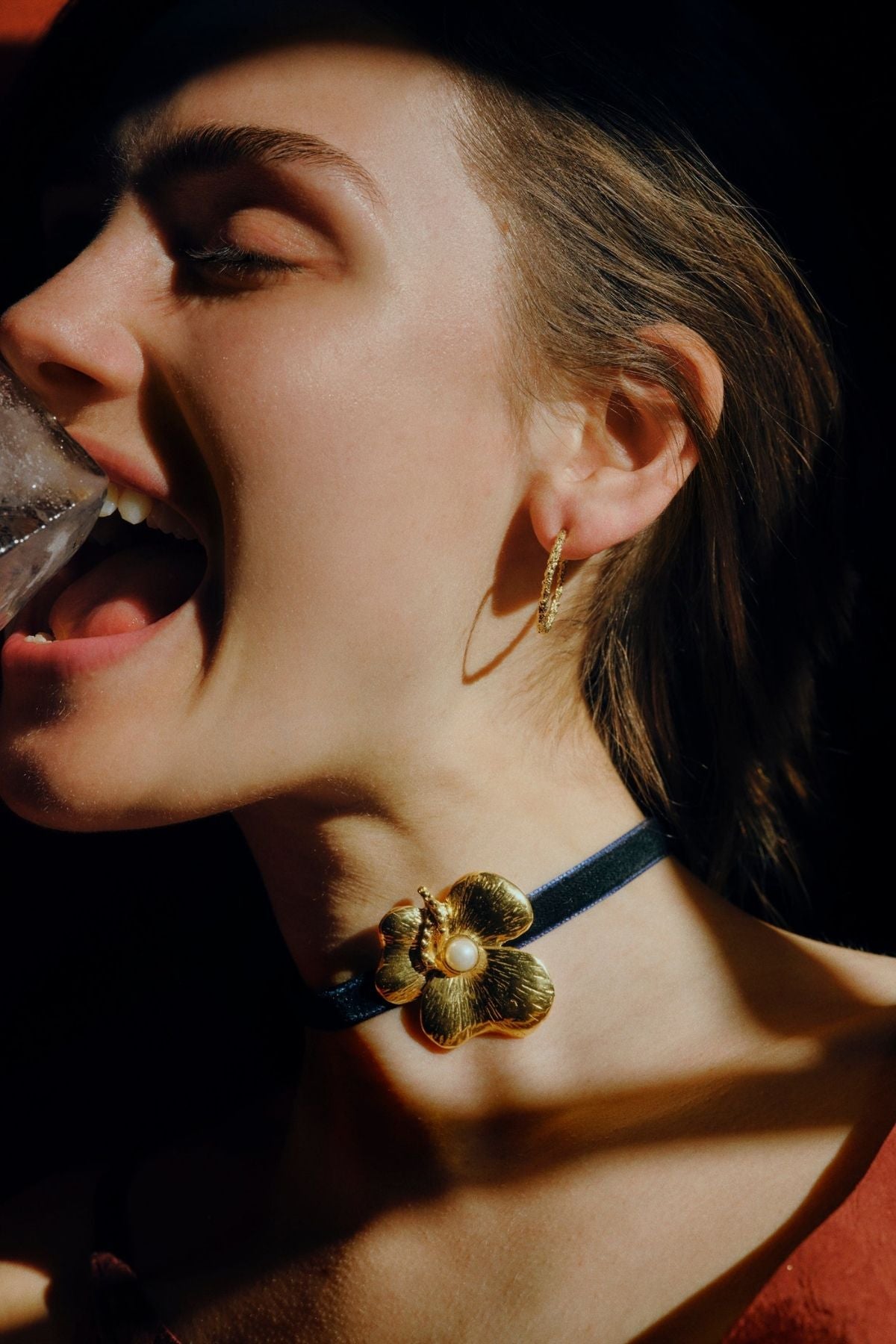 Close-up of a person wearing a gold earring and a necklace with a floral design.