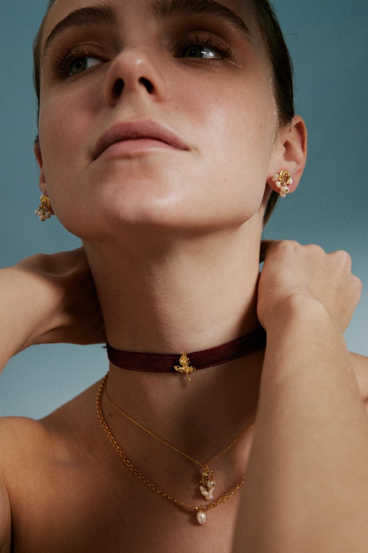 Woman wearing gold necklaces and earrings against a blue background