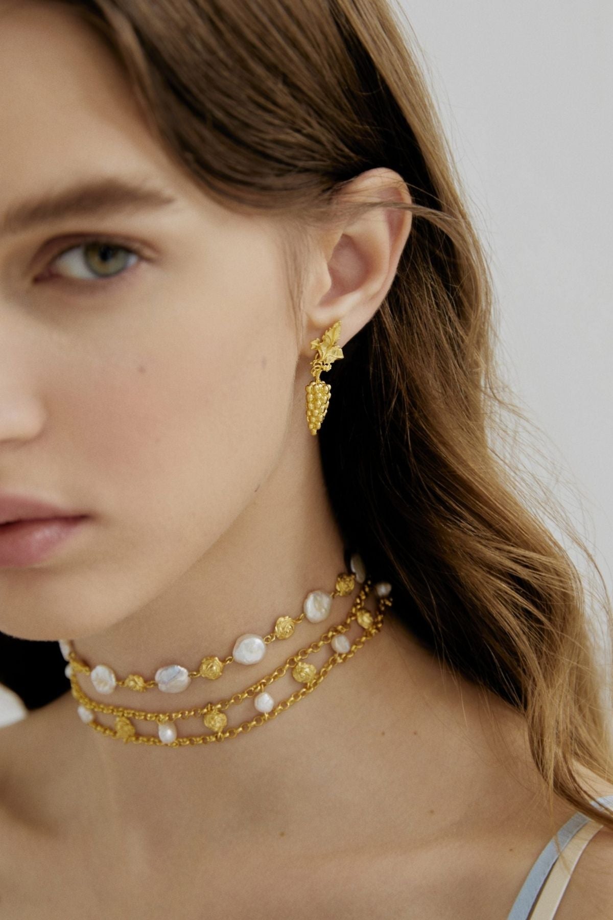 Close-up of a woman wearing gold earrings and necklaces against a neutral background