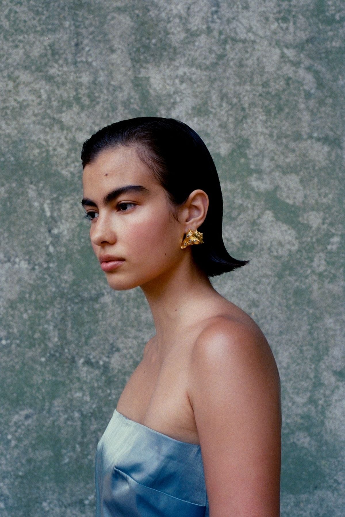 Woman wearing gold earrings against a textured gray background