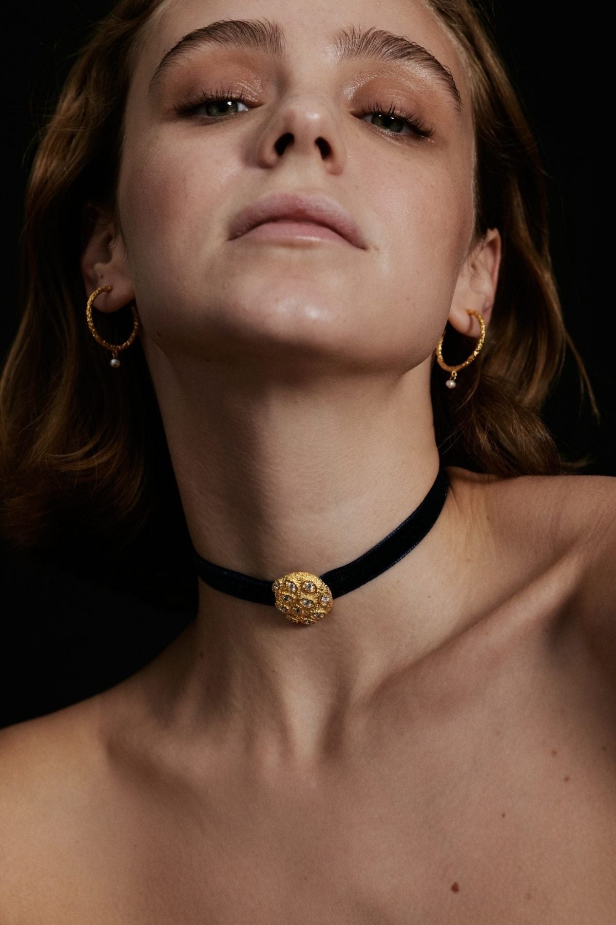 Woman wearing a black choker with a gold pendant against a dark background