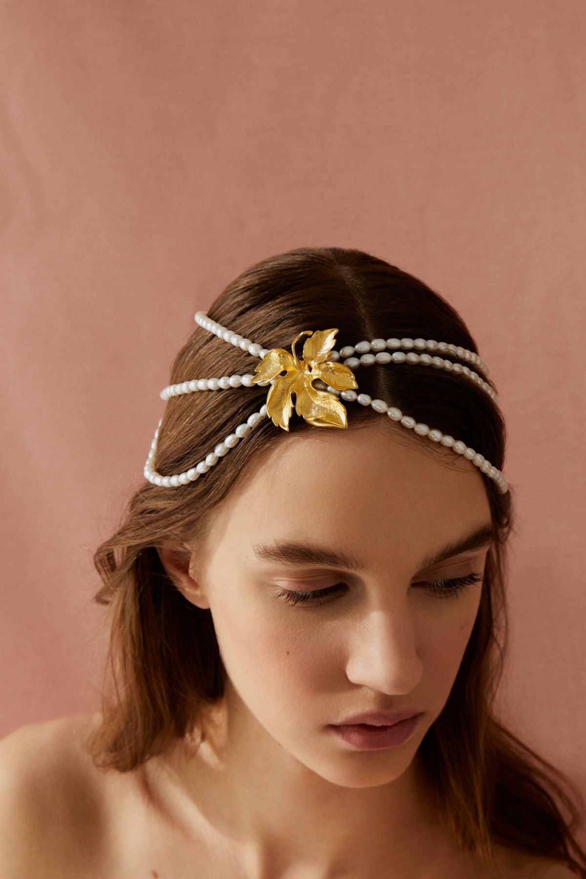 Woman wearing a gold leaf headband with pearl-like strings on a pink background
