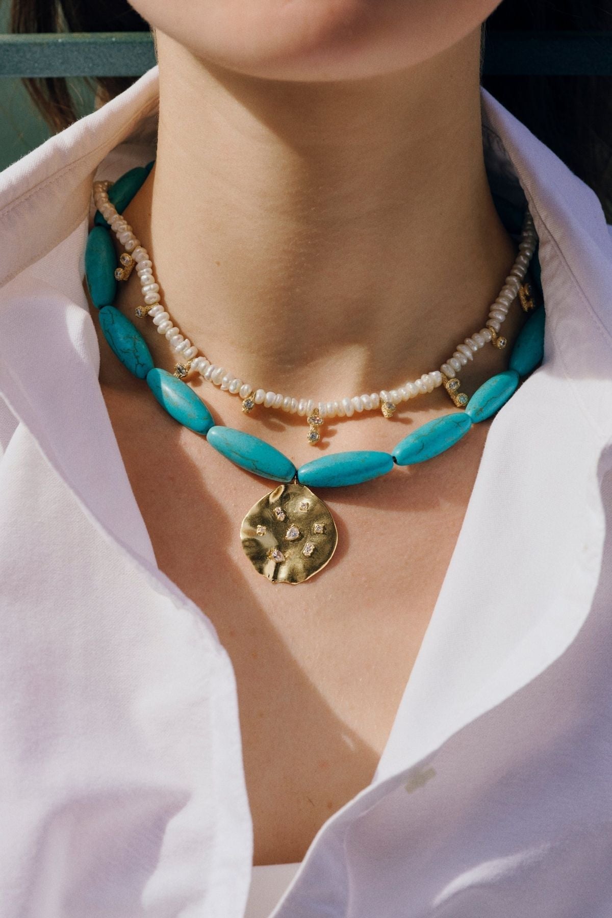 Close-up of a person wearing a turquoise beaded necklace with a gold pendant.