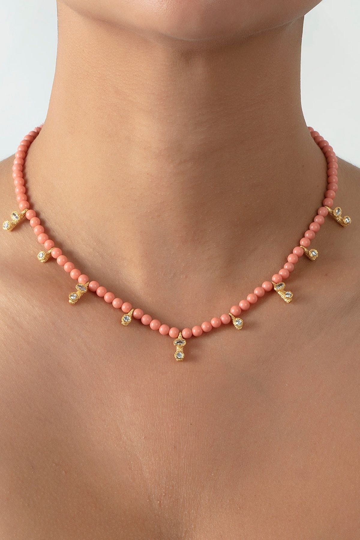 Necklace with pink beads and gold accents on a person's neck against a neutral background