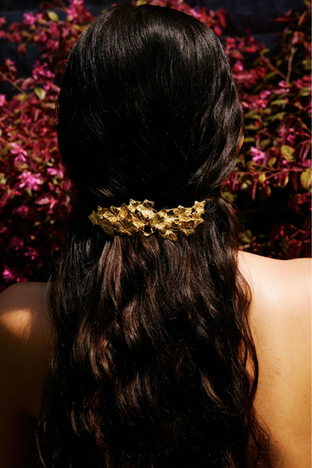 Woman with long dark hair wearing a gold headband against a blurred floral background