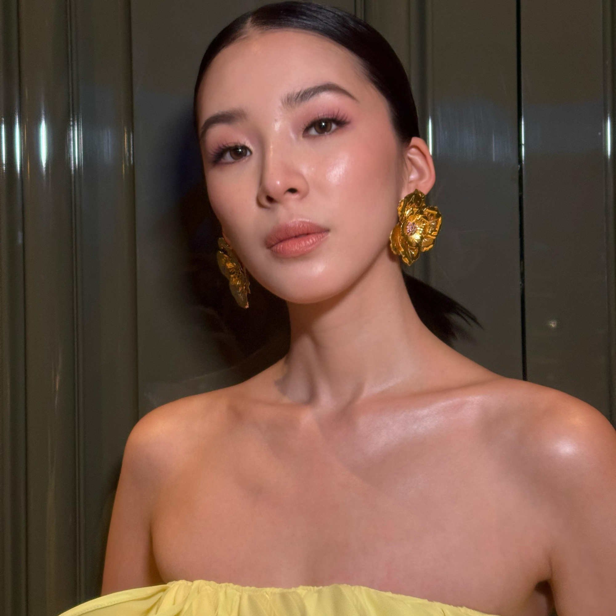 Woman wearing a yellow strapless top and gold earrings against a neutral background