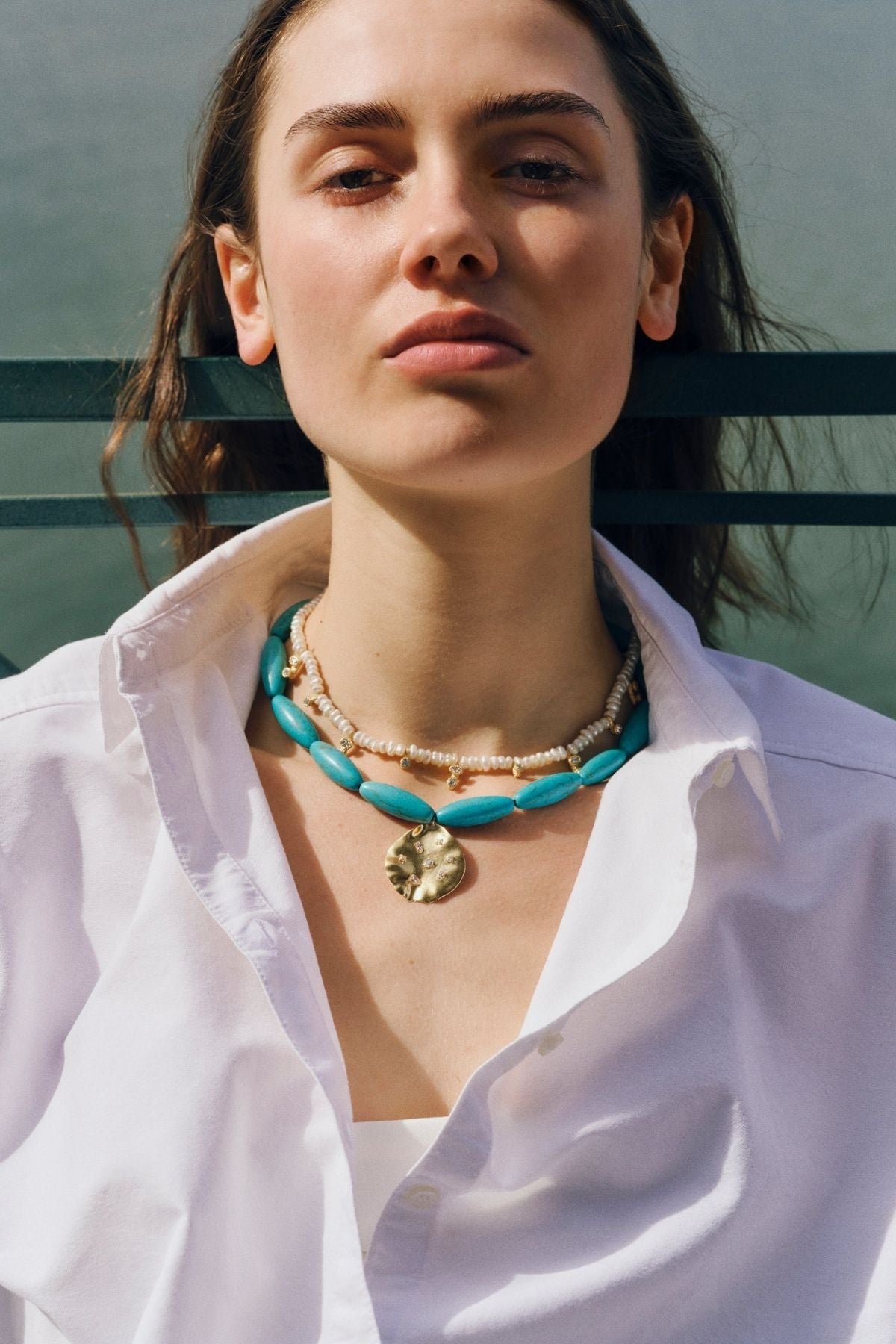 Woman wearing a white shirt and multiple necklaces with a blurred background