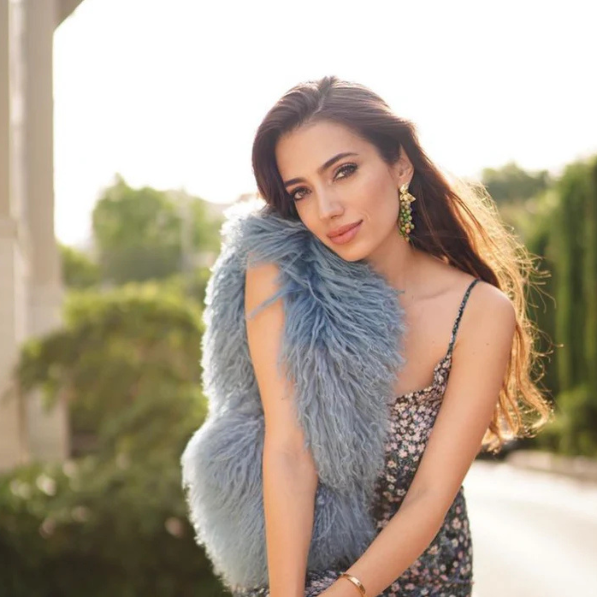 Woman wearing a blue fur vest outdoors with greenery in the background